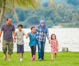 A Malaysian muslim family holding each other hands and walking in a row at the park.